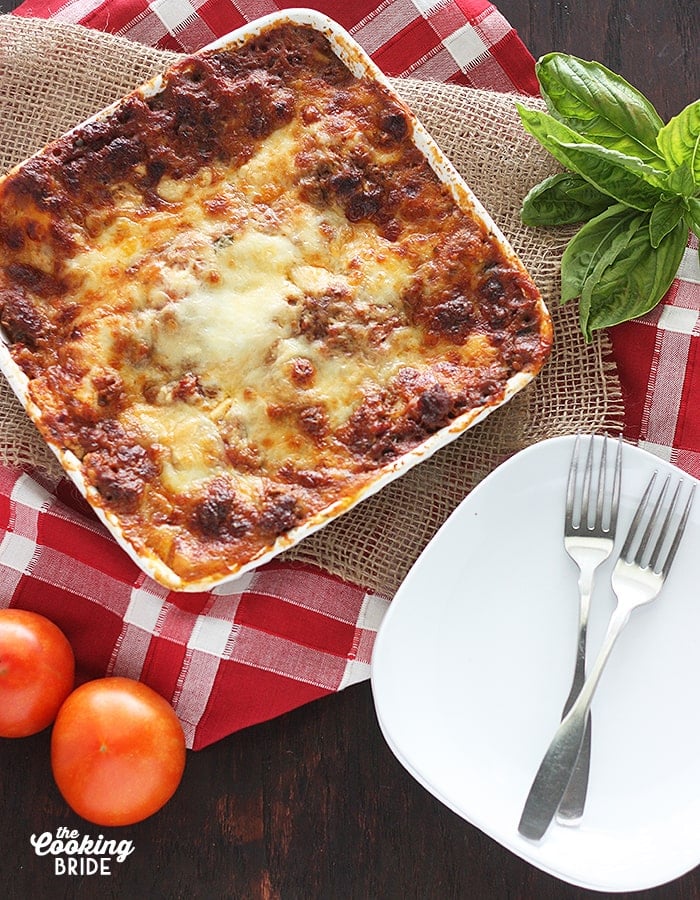 overhead shot of baked lasagna in a white casserole dish with a white plate and forks on the side
