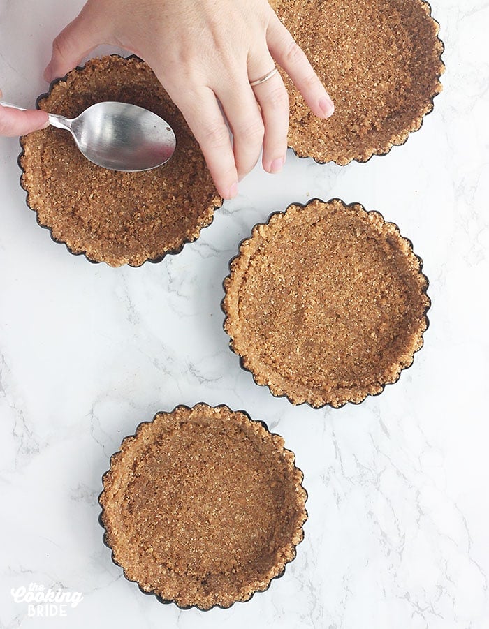 set of hands pressing the graham cracker crust into mini tart pans