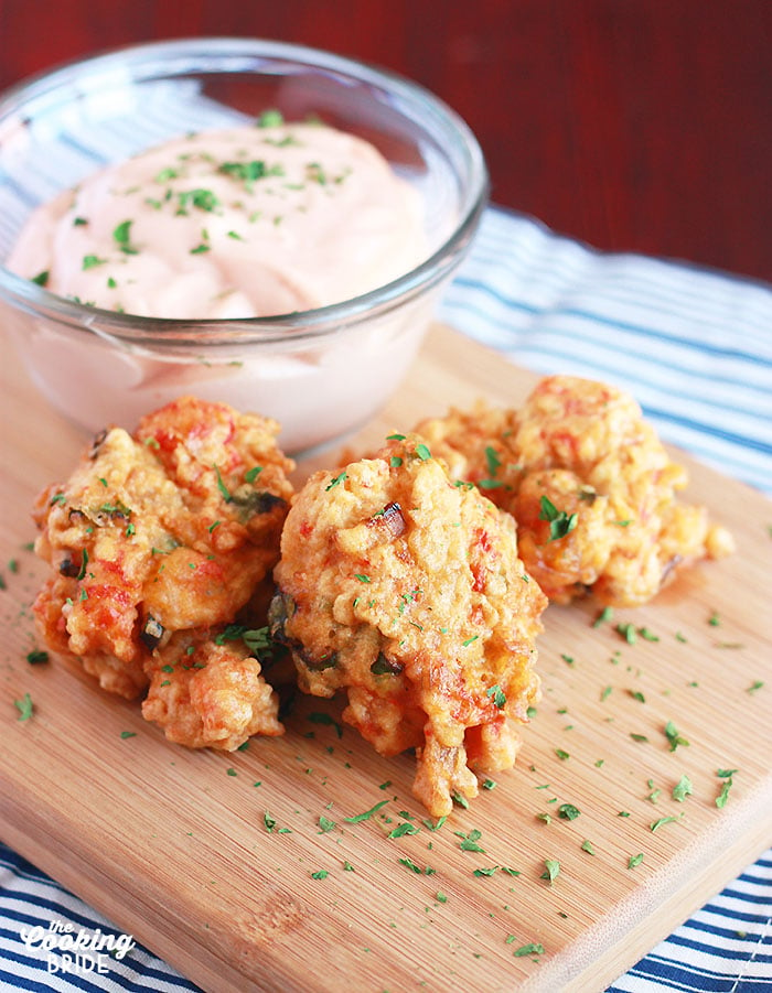 three crawfish beignets on a wooden board with sauce in the background