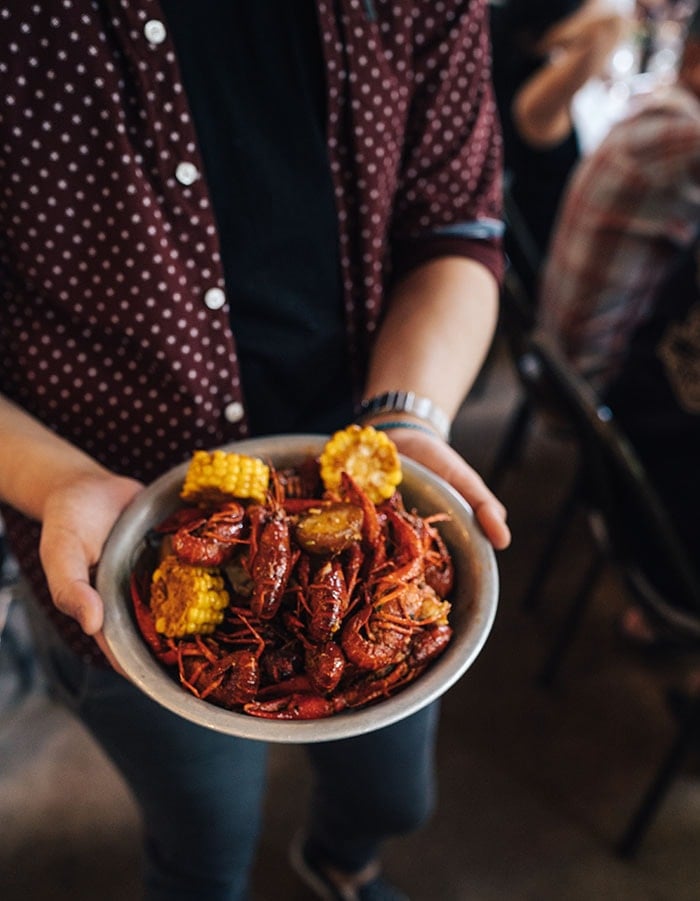 person holding a bowl of crawfish and corn