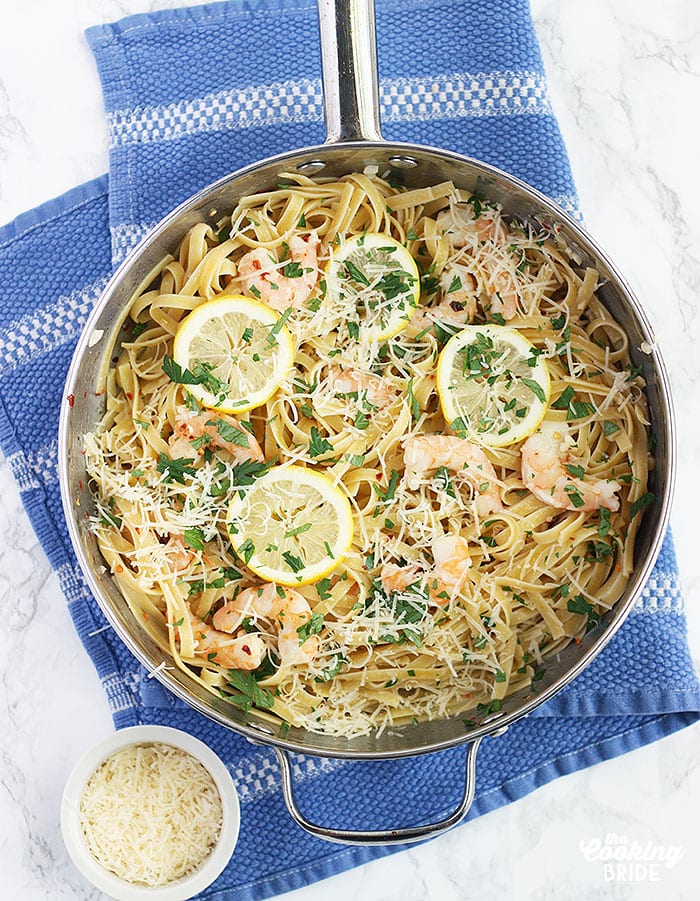 Fettuccine noodles topped with shrimp scampi in a stainless steel pan