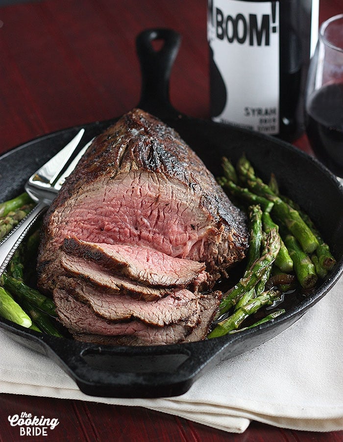sliced roast beef on surrounded by roasted asparagus in a cast iron pan.