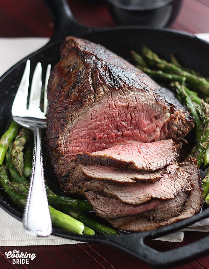 sliced medium rare roast beef with roasted asparagus sitting in a cast iron skillet