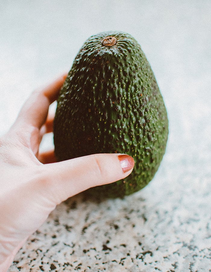 lady's hand holding an avocado upright on a countertop