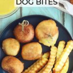 Five mini corndog bites on a plate with crinkle cut French fries. Half of one corndog bite is coated in honey mustard sauce. A dish of honey mustard sauce, ketchup and toothpicks are to the side of the plate.