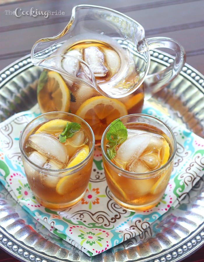 a glass pitcher of sweet tea with lemon and two serving glasses on a pewter tray with a multicolored napkin