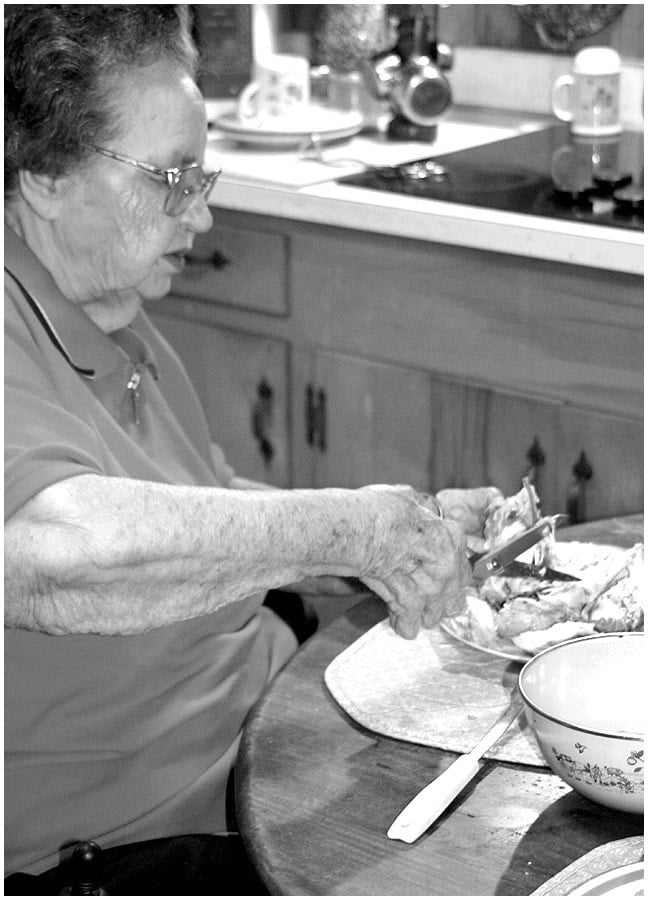 Mamaw sitting at her kitchen table cutting up chicken for her homemade chicken and dumplings.