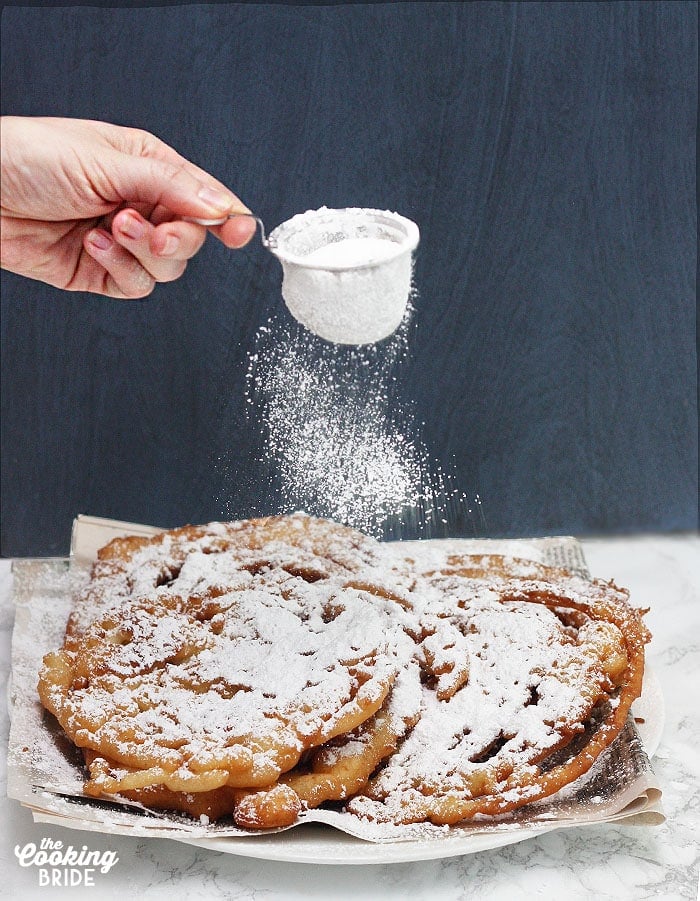 sprinkling powdered sugar over the funnel cakes