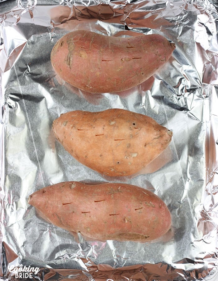 Unbaked sweet potatoes with holes on a foil lined baking sheet.