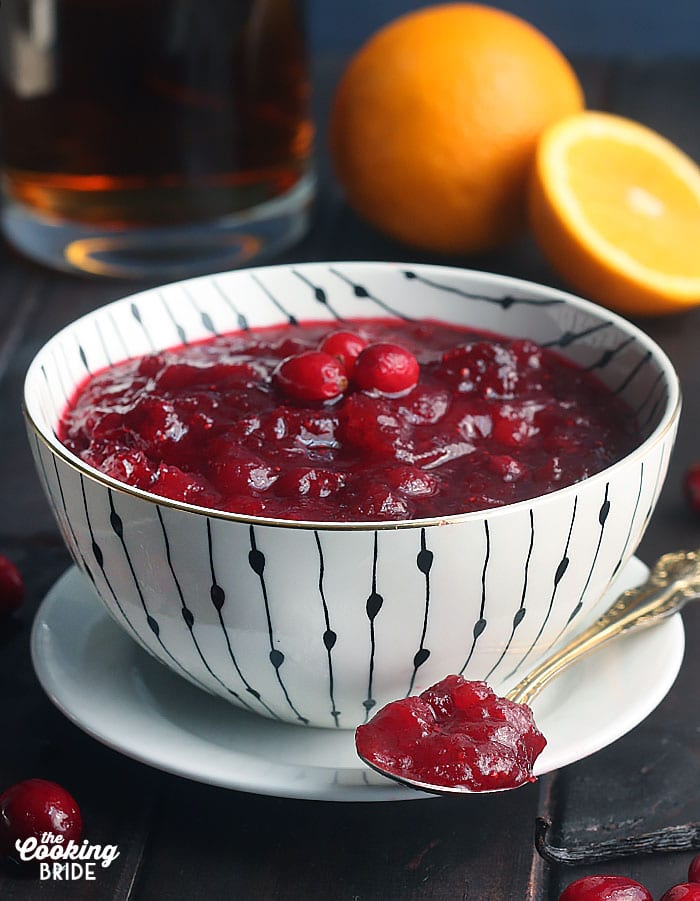 fresh cranberry sauce in a white and black bowl with a spoon of sauce resting on a saucer to the side