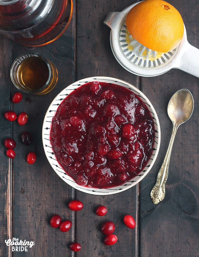 overhead shot of fresh cranberry sauce on a wooden background surrounded by fresh cranberries, a shot of bourbon and fresh orange 