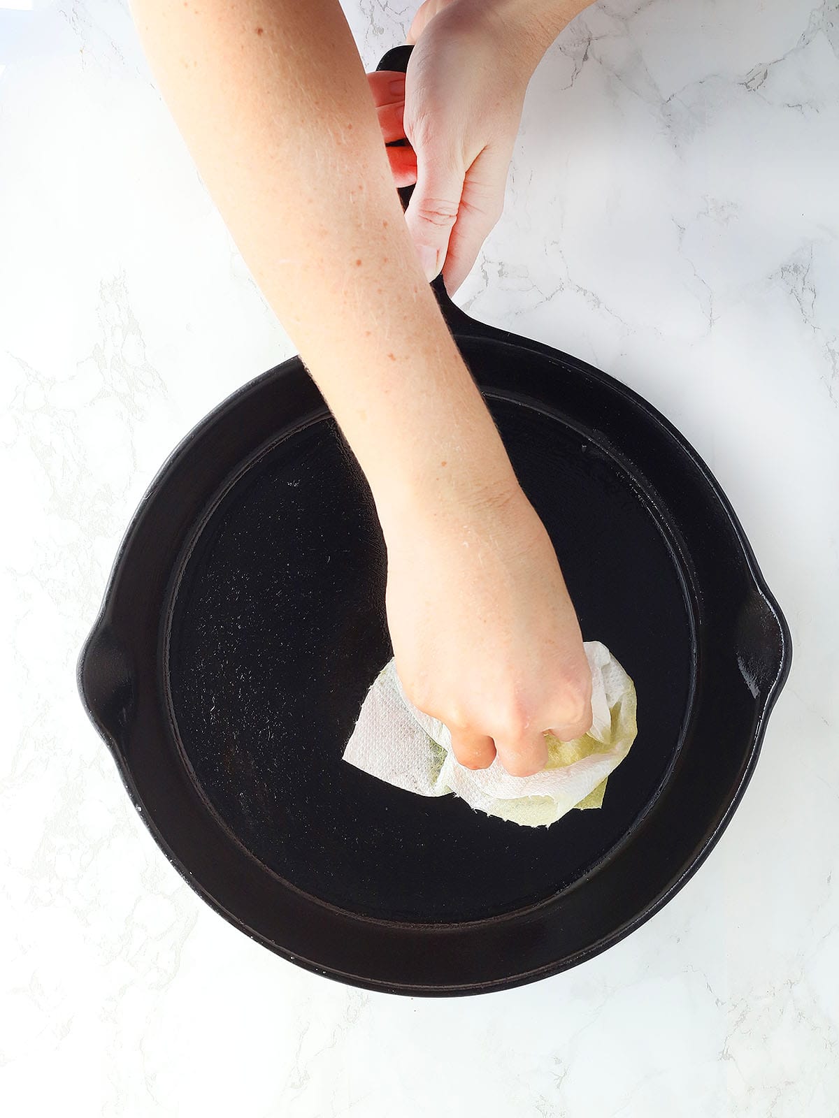 hand wiping excess oil out of a cast iron skillet