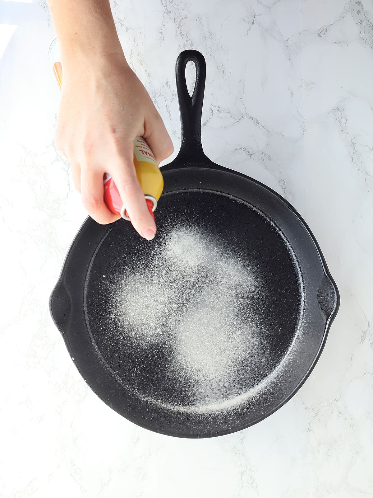 Hand spraying a cast iron skillet with cooking spray.