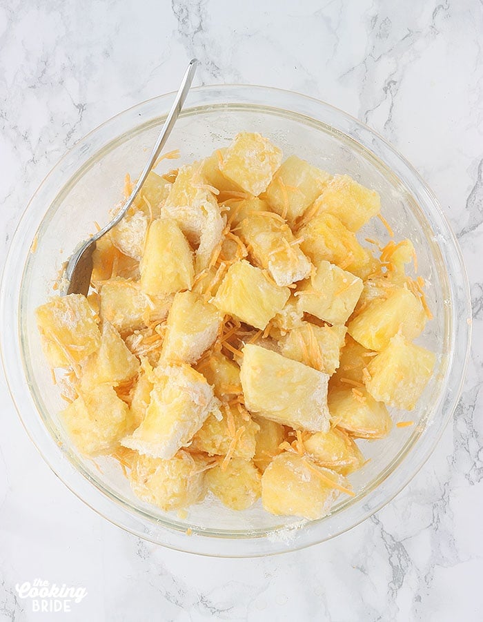 pineapple chunks in a large glass mixing bowl combined with cheese, flour and sugar