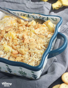 baked pineapple casserole in a blue and white casserole dish on a gray napkin