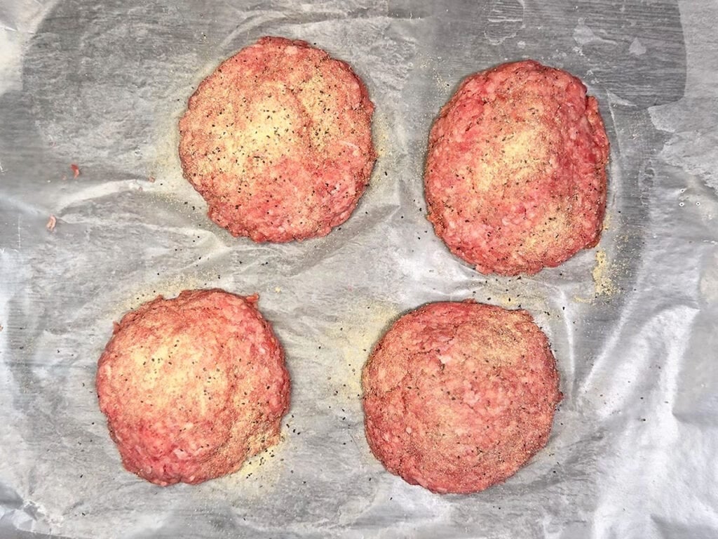 Seasoning the outside of the stuffed burger patties.