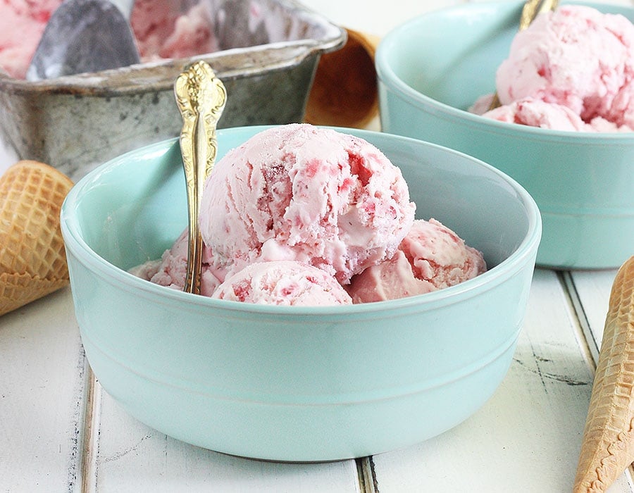 strawberry ice cream in a light blue bowl against a white wooden background.
