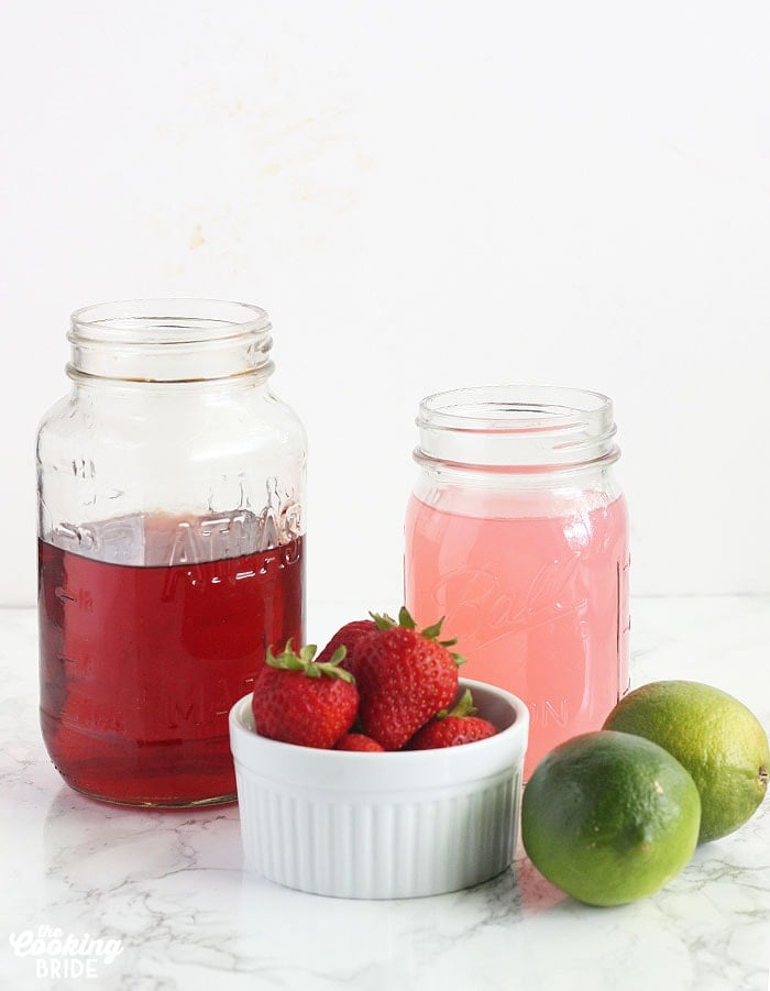 lemonade ingredients including cherry vodka and pink lemonade in a mason jar, fresh limes and fresh strawberries
