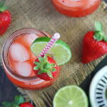 overhead shot of two glasses of vodka lemonade on a wooden background with strawberries and limes surrounding the glasses