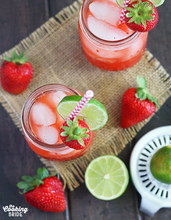 overhead shot of two glasses of vodka lemonade on a wooden background with strawberries and limes surrounding the glasses 