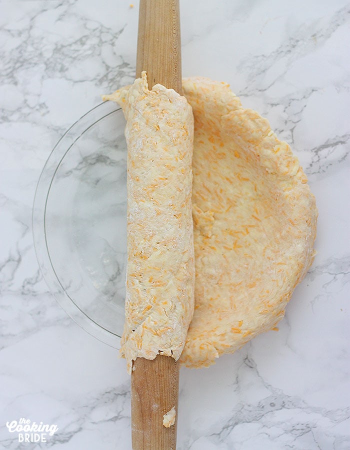 using a rolling pin to roll the cheddar cheese crust into the pie plate