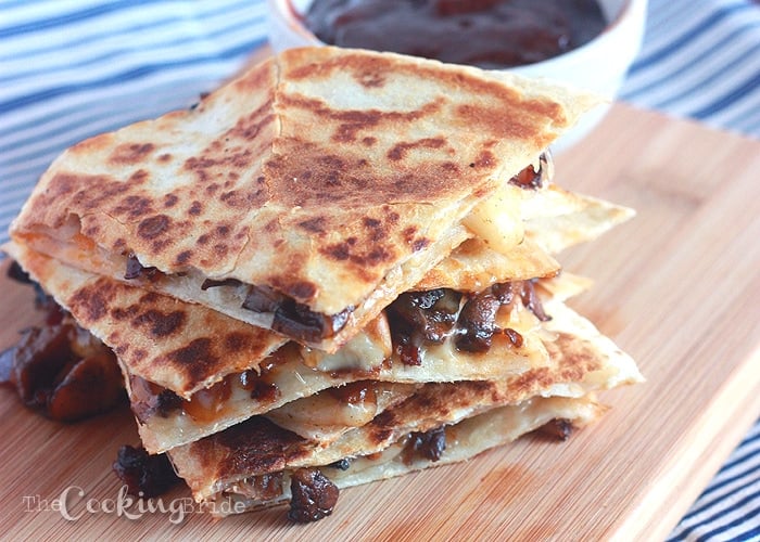 Mushroom Quesadillas  stacked on a wooden cutting board with a bowl of barbecue sauce in the background