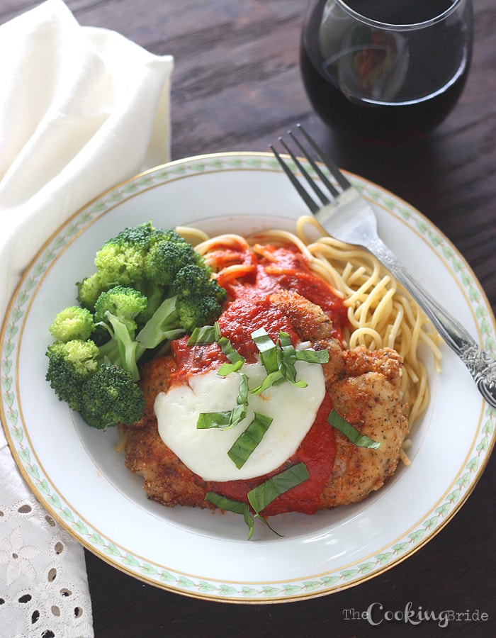 chicken parmesan on a white plate with a glass of rec wine in the background