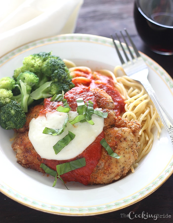 chicken parmesan on a white plate with a glass of rec wine in the background