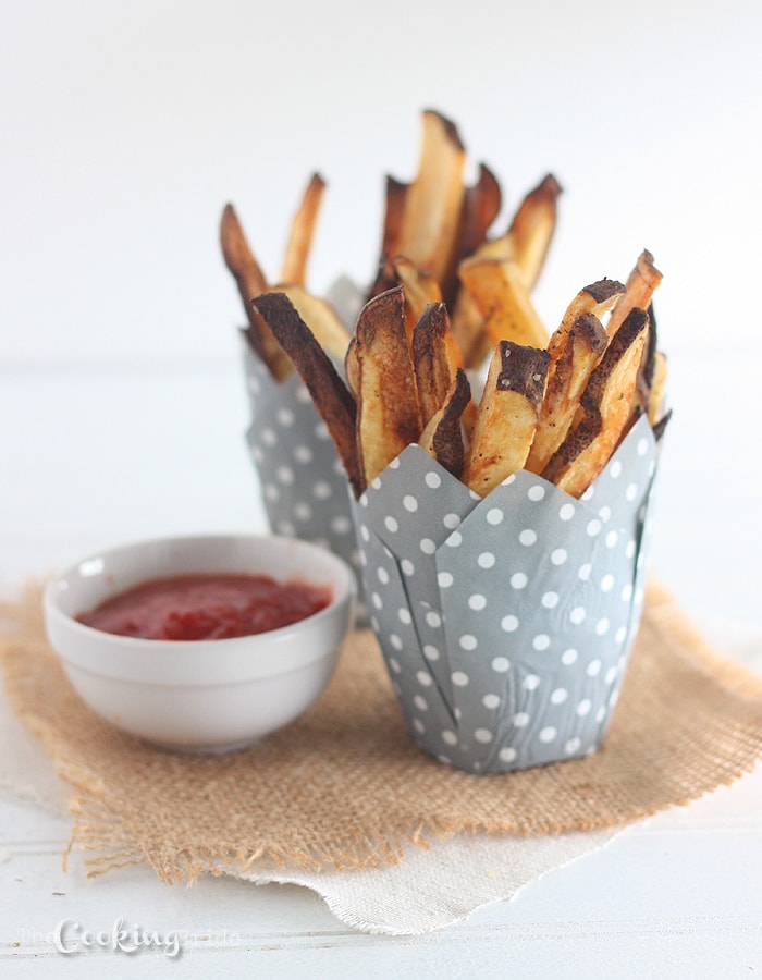 french fries in a gray polka dot paper cup with a small bowl of ketchup on the side.