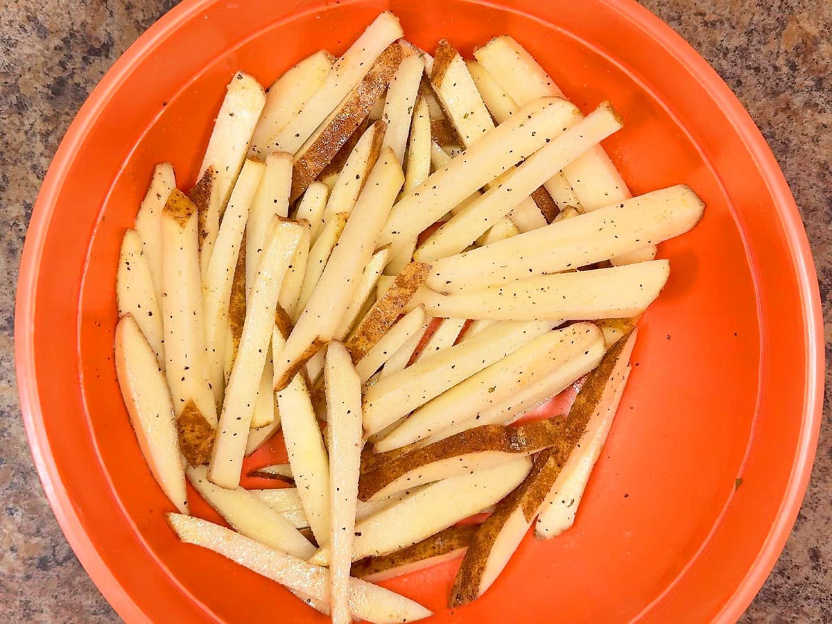 Oiled and seasoned cut potatoes in a large bowl.