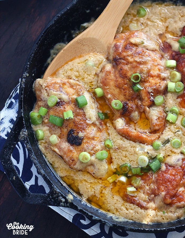 close up of a piece of paprika chicken nestled in gravy in a cast iron skillet with a wooden spoon