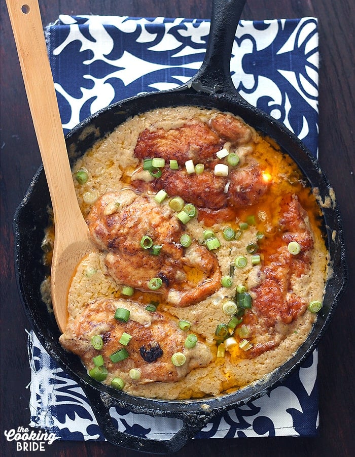 paprika chicken nestled in gravy in a cast iron skillet with a wooden spoon