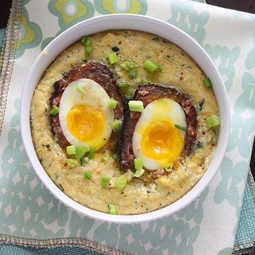 Easy to make scotch egg recipe is the perfect brunch! Soft boiled eggs are wrapped in sausage, dredged in Panko breadcrumbs, the fried until golden brown. Served over creamy, buttered herb corn grits.