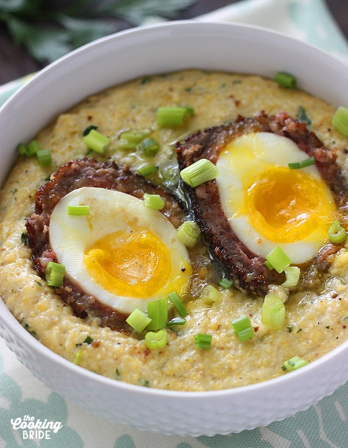 close up shot of a scotch egg nestled in a bowl of corn grits sprinkled with green onions