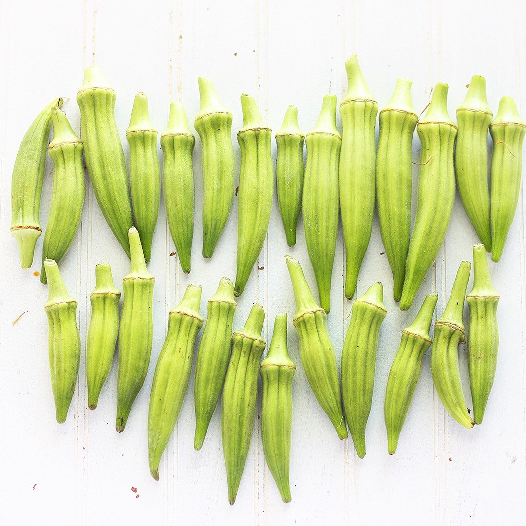 fresh okra pods arranged in rows o a white background