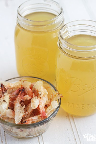 two mason jars of shrimp stock next to a bowl of shrimp shells