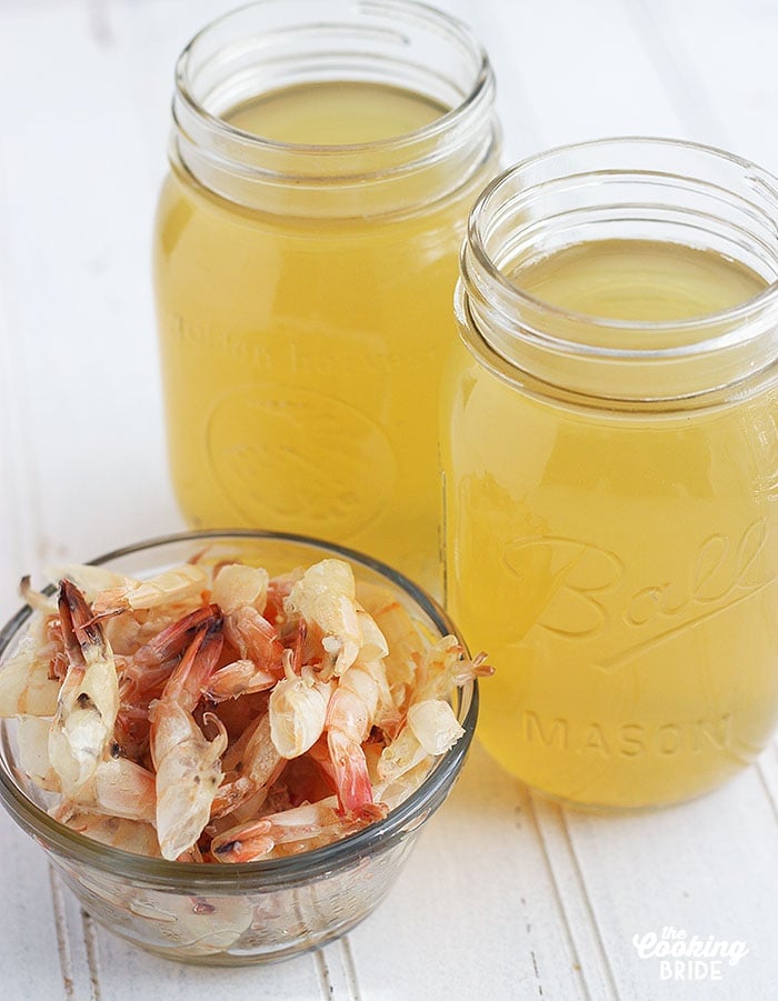 two mason jars of shrimp stock next to a bowl of shrimp shells