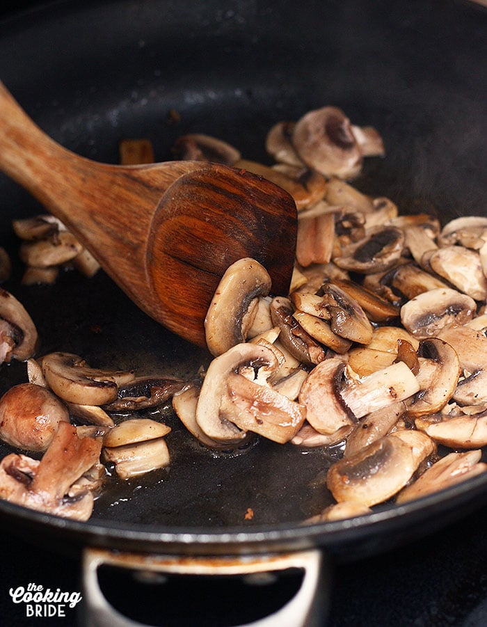 stirring mushrooms in a skillet