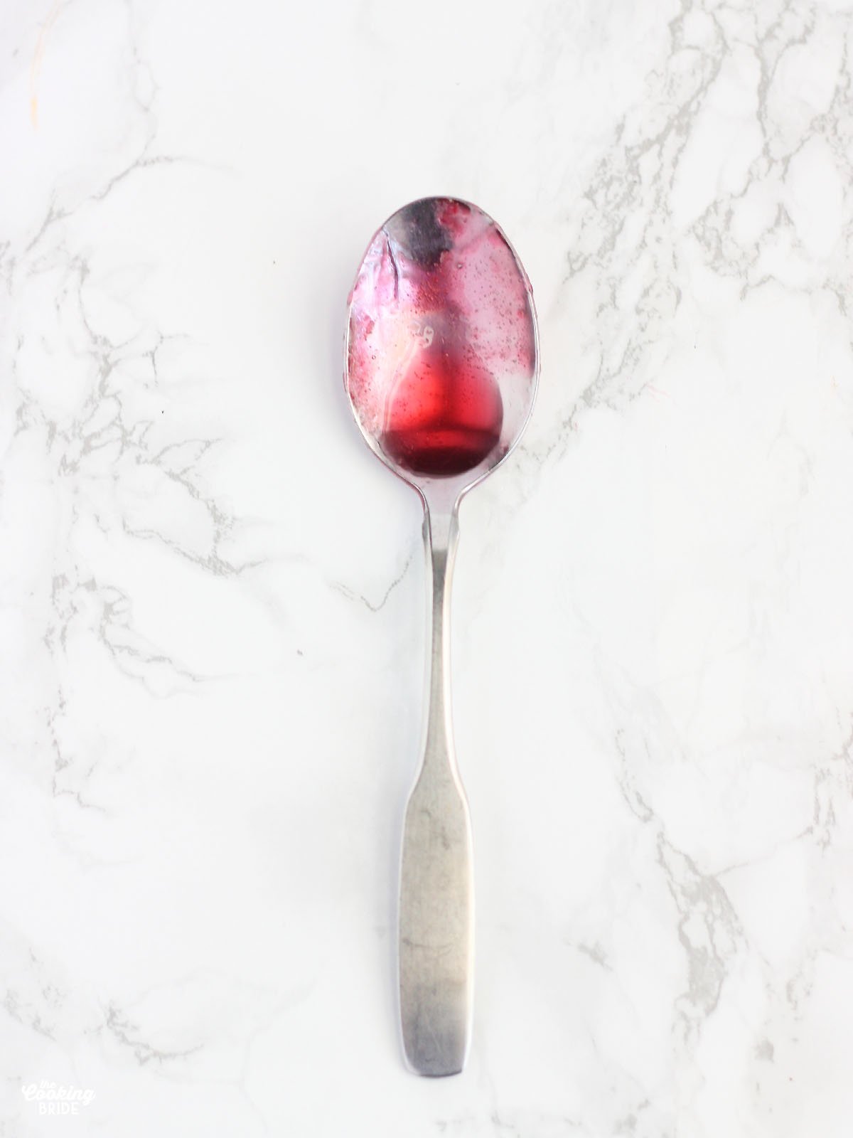 metal spoon covered with a drop of plum jelly on it