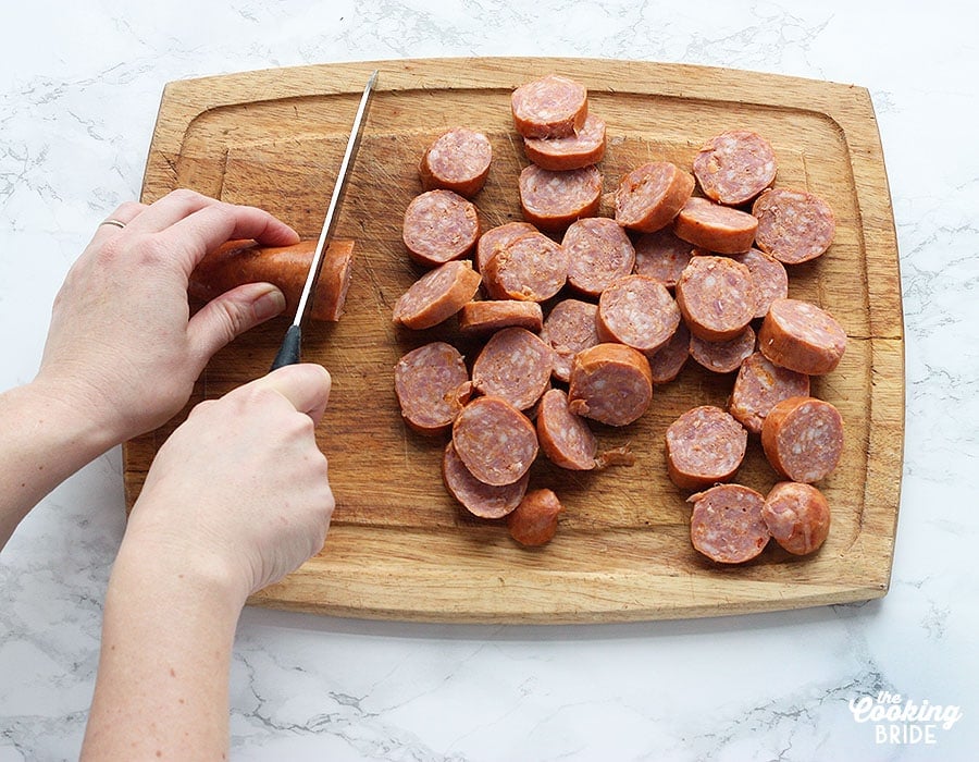 pair of hands slicing andouille sausage on a wooden cutting board