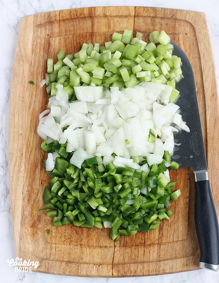 diced celery, onions and green bell peppers on a cutting board with a knife