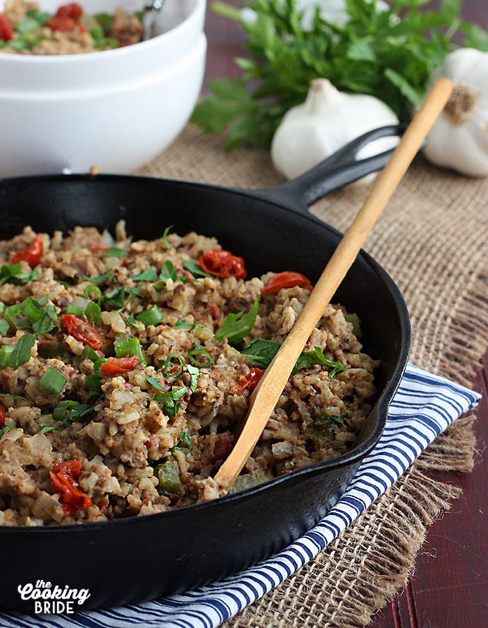 side view of finished cajun dirty rice in a cast iron skillet with a wooden spoon