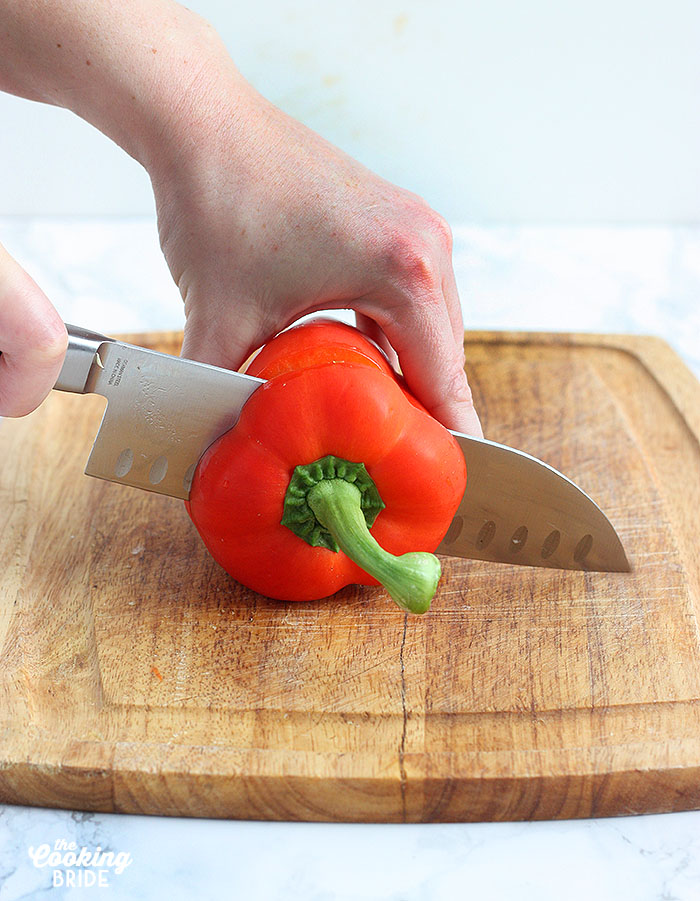hand slicing into a red bell pepper on a wooden cutting board