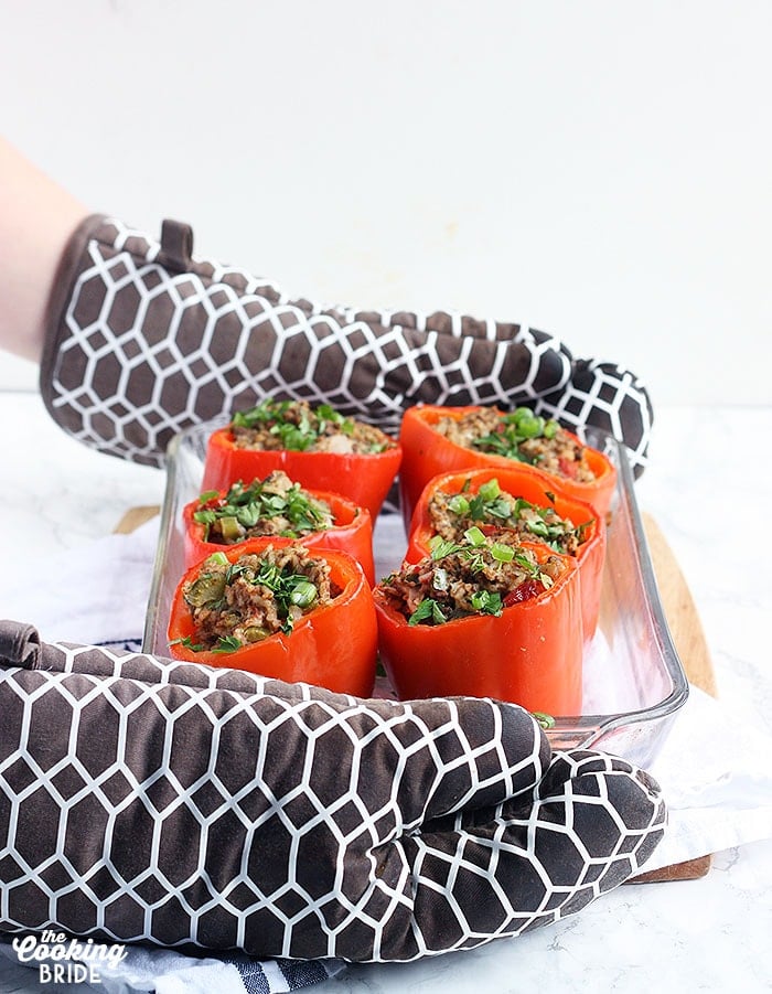 pair of hands in oven mits setting down a dish of stuffed bell peppers