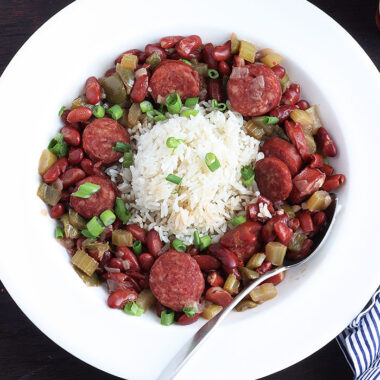 White dish of red beans and rice with a metal spoon, bowl of cooked rice and an Instant pot to the side.
