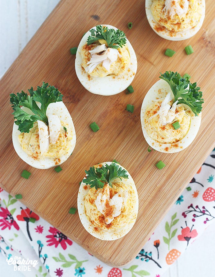 four crab deviled eggs on a wooden cutting board