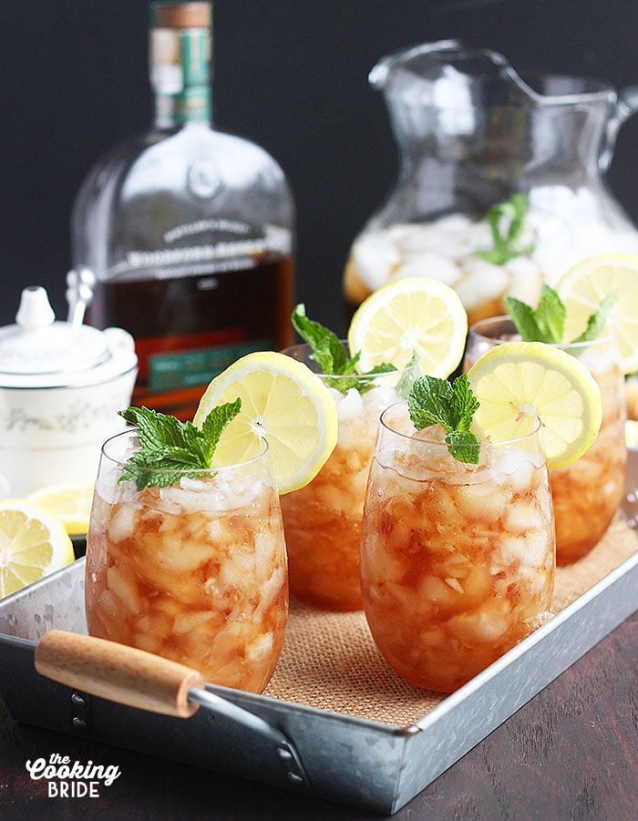 mint julep cocktails on a metal tray with a bottle of bourbon and sweet tea in the background