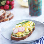 egg salad sandwich on a gray plate garnished with radishes and chives
