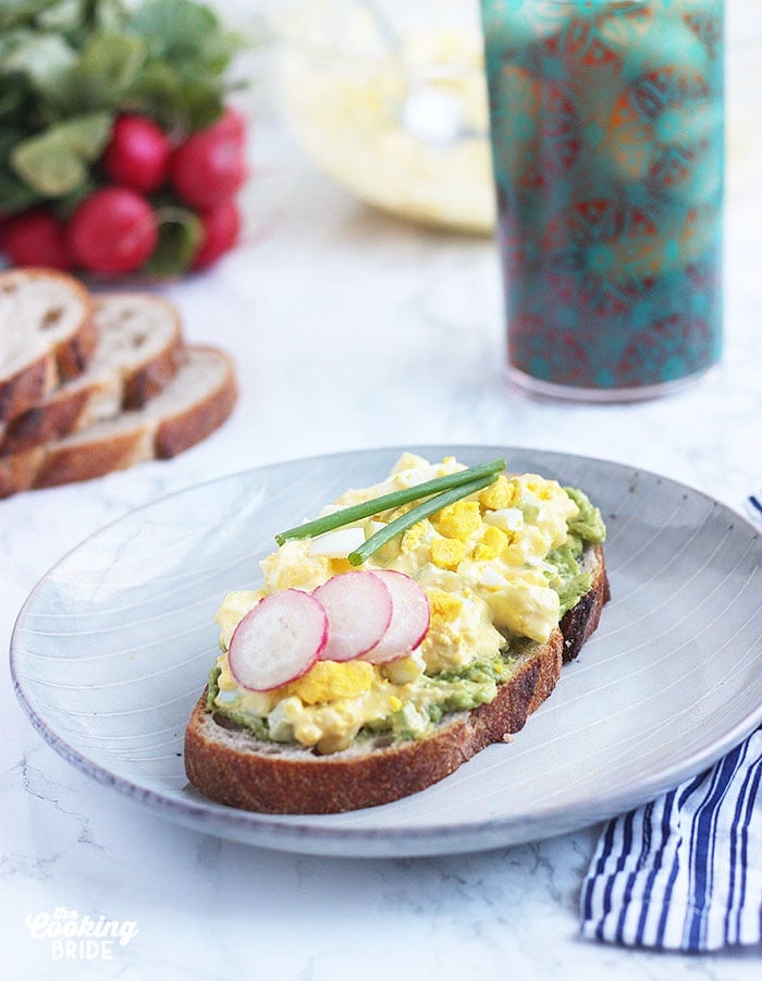 egg salad sandwich on a gray plate garnished with radishes and chives