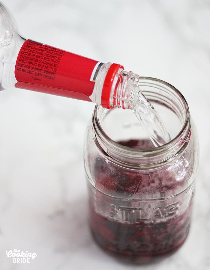 pouring vodka into a cherry filled mason jar